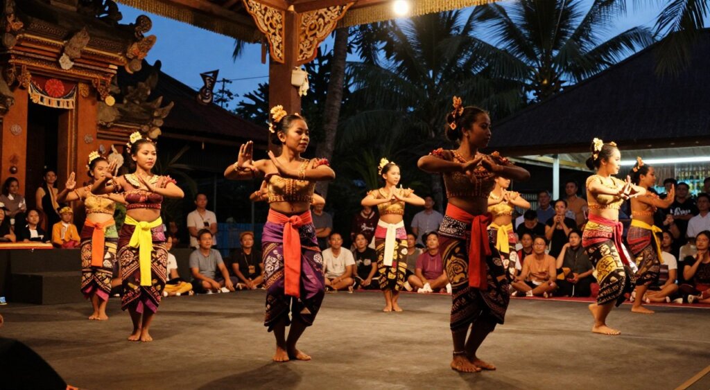 A vibrant traditional Kuta dance performance set against a backdrop of a dimly lit open-air stage adorned with intricate Balinese decorations. In the foreground, a group of dancers in colorful traditional attire gracefully moves, showcasing expressive hand gestures and intricate footwork, illuminated by warm, soft lighting that highlights their faces and costumes. The middle layer includes captivated audience members, some seated on mats, immersed in this cultural spectacle, capturing the mood of awe and appreciation. In the background, palm trees are silhouetted against a twilight sky, adding to the lush ambiance of the tropical setting. The scene is shot with a slightly low angle to emphasize the energy and movement of the dancers, creating a dynamic composition that embodies the spirit of Kuta's rich cultural heritage.